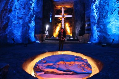 In einer beeindruckenden Salzkathedrale steht eine Person vor einer beleuchteten Statue, umgeben von blauen Felsen und warmem Licht.