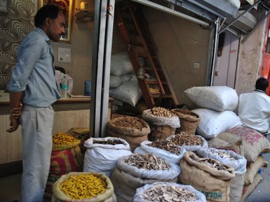 Ein Mann steht neben einem Stapel von Säcken mit verschiedenen Gewürzen in einem geschäftigen Markt in Delhi.