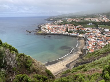 Ein Blick auf eine malerische Küstenstadt mit bunten Häusern, die sich entlang des Wassers erstrecken, umgeben von sanften Hügeln.