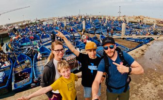 Familie macht Selfie vor blauen Fischerbooten im Hafen von Essaouira – Marokko Familienreise