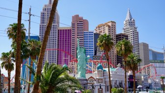 Die Freiheitsstatue steht stolz im Vordergrund, umgeben von Palmen und bunten Wolkenkratzern in Las Vegas.