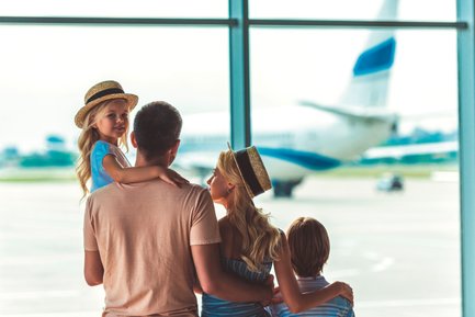 Eine Familie steht am Flughafen und beobachtet ein Flugzeug, während das kleine Mädchen auf dem Arm des Vaters sitzt.