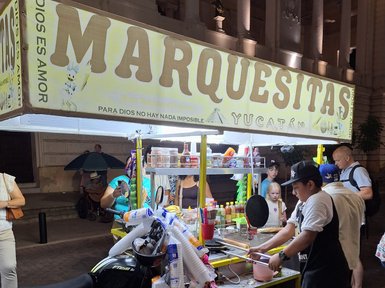 Ein Straßenverkäufer bereitet frische Marquesitas an einem bunten Stand in Yucatán vor, umgeben von neugierigen Passanten.