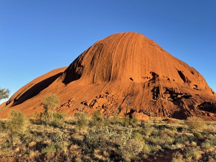 Die majestätische Form des Ayers Rock erhebt sich imposant gegen den klaren, blauen Himmel in der australischen Wüste.