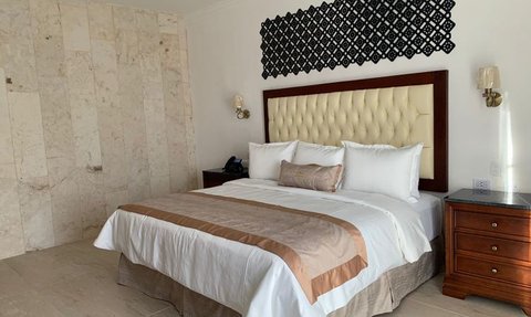 Ein elegantes Schlafzimmer mit einem großen Bett, das mit weißen und beigen Kissen dekoriert ist, und einer stilvollen Wandverkleidung.