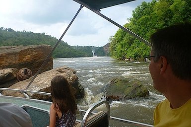 Ein Kind und ein Erwachsener genießen eine Bootsfahrt auf einem Fluss, während im Hintergrund ein Wasserfall zu sehen ist.