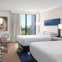 Ein modernes Hotelzimmer mit zwei Betten, eleganten Möbeln und großen Fenstern, die Tageslicht hereinlassen.