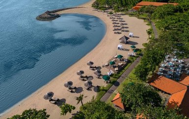 Ein malerischer Strand mit Sonnenliegen und Sonnenschirmen, umgeben von üppigem Grün und klarem Wasser.