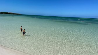 Zwei Jungen stehen im flachen Wasser eines klaren Strandes, umgeben von sanften Wellen und strahlend blauem Himmel.