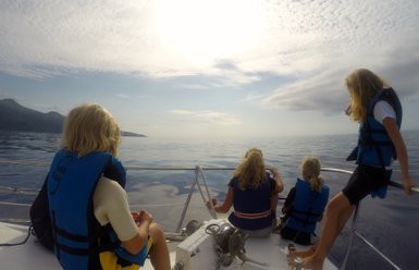 Eine Gruppe von Kindern in Schwimmwesten beobachtet das ruhige Wasser und die Küste im Hintergrund, während sie auf einem Boot sitzen.