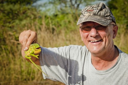 Ein lächelnder Mann hält eine bunte Froschart in der Hand, umgeben von einer grünen, natürlichen Umgebung.