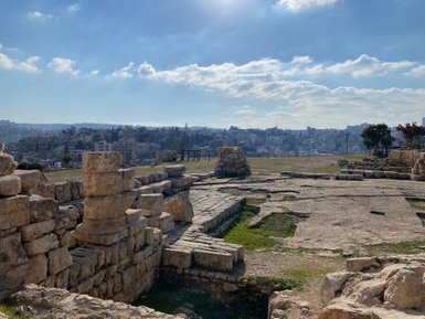 Die Ruinen eines antiken Tempels sind im Vordergrund sichtbar, während die Stadt Amman im Hintergrund liegt.
