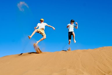 Kinder genießen die Freiheit und springen voller Freude auf den weiten Sanddünen der Wüste – Marokko Reise mit Kindern