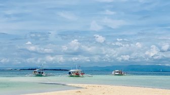 Drei traditionelle philippinische Auslegerboote gleiten sanft über das klare Wasser, umgeben von einem strahlend blauen Himmel.