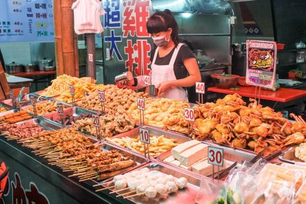 Eine Verkäuferin in einem Streetfood-Markt bereitet eine Vielzahl von frittierten Snacks und Meeresfrüchten vor.