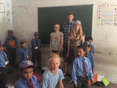 Eine Gruppe von Kindern in Schuluniformen steht in einem Klassenzimmer, umgeben von Lehrmaterialien und einem Lehrer.