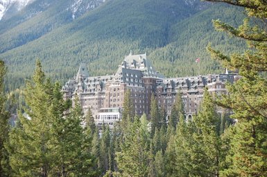 Das Fairmont Banff Springs Hotel thront majestätisch zwischen hohen, grünen Bäumen und majestätischen Bergen im Hintergrund.