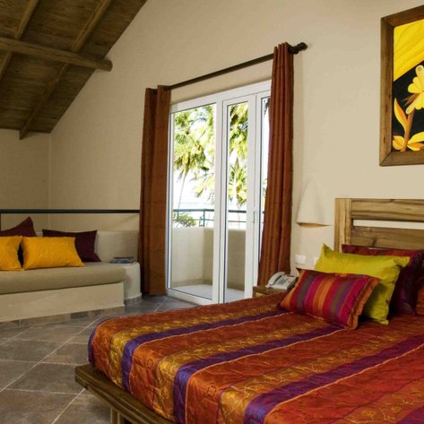 Ein helles Schlafzimmer mit einem großen Bett, bunten Kissen und einem Fenster, das auf eine grüne Landschaft blickt.