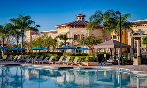 Ein einladender Poolbereich mit Liegen und Sonnenschirmen, umgeben von Palmen und einem eleganten Gebäude im Hintergrund.