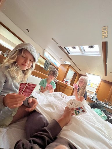 Vier Kinder sitzen in einem Boot und spielen Karten, während sie sich unter einer Decke entspannen und lachen.