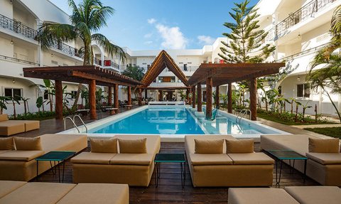 Ein einladender Poolbereich mit modernen Liegen und einem schattigen Pavillon, umgeben von tropischen Pflanzen und klarem Himmel.