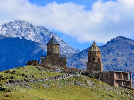 Eine beeindruckende Berglandschaft mit schneebedeckten Gipfeln und einer historischen Kirche auf einem Hügel.