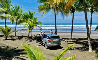 Am Strand von Playa Quepos stehen vier Personen, die das Ocean-View bewundern, während ein Auto im Sand parkt.