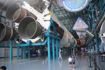 Im Kennedy Space Center stehen zwei Kinder fasziniert vor einem riesigen Raketenmotor, während Besucher im Hintergrund umhergehen.