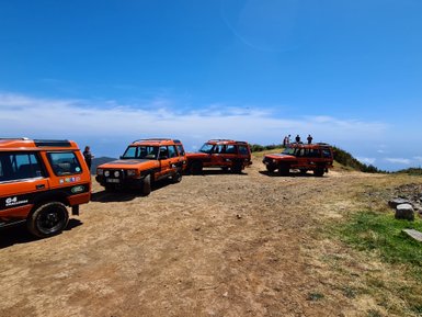 Eine Gruppe von orangefarbenen Geländewagen steht auf einem staubigen Weg mit Blick auf eine weite Landschaft und blauen Himmel.