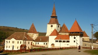 Eine malerische Burg mit roten Dächern und einem hohen Turm, umgeben von sanften Hügeln und klarem blauen Himmel.