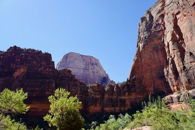 Majestätische Felsen erheben sich unter einem strahlend blauen Himmel im Zion-Nationalpark, umgeben von üppigem Grün.