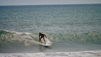 Ein Surfer balanciert geschickt auf seinem Surfbrett, während er eine Welle im ruhigen Wasser reitet.