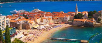 Eine malerische Küstenstadt mit roten Dächern, umgeben von klarem, blauem Wasser und sanften Hügeln im Hintergrund.