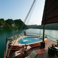 Ein luxuriöses Kreuzfahrtschiff mit einem Whirlpool auf dem Deck, umgeben von grünen Inseln und klarem Wasser.