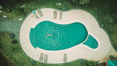 Ein Schwimmer entspannt in einem ausladenden Pool, umgeben von Sonnenliegen und üppiger Pflanzenwelt.