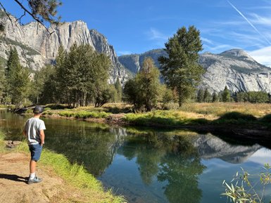 Ein Junge steht am Ufer eines ruhigen Gewässers und betrachtet die majestätischen Berge im Hintergrund.