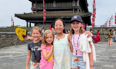 Vier Mädchen stehen fröhlich vor einem historischen Torturm in Xi'an und lächeln in die Kamera, während bunte Laternen im Hintergrund schweben.