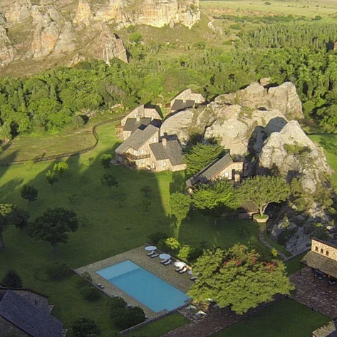 Eine malerische Landschaft mit Felsen, üppigem Grün und einem klaren Pool, umgeben von charmanten, rustikalen Gebäuden.