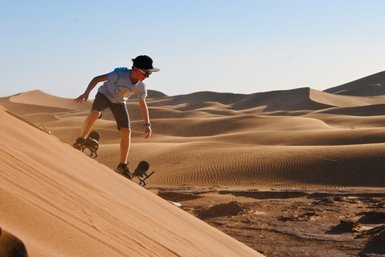 Kind gleitet mit einem Sandboard die sandigen Dünen der Wüste hinunter – Familienreise nach Marokko