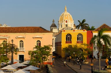 Bunte Gebäude umgeben den Platz, während Menschen und Motorräder die lebhafte Atmosphäre von Cartagena genießen.