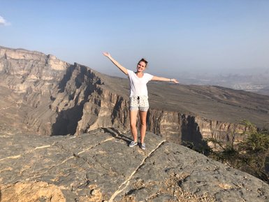 Mädchen steht auf einem Felsen mit Blick auf die zerklüftete Landschaft des Jebel Shams – Oman Familienreise