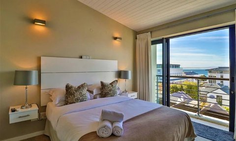 Ein elegantes Hotelzimmer mit einem großen Bett, dekorativen Kissen und Blick auf das Meer durch große Fenster.