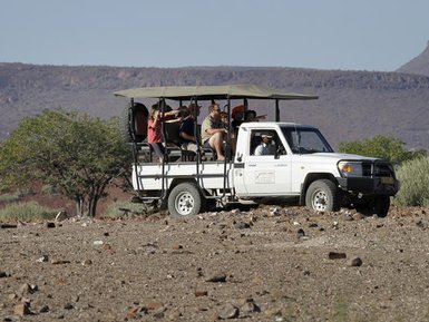 Eine Gruppe von Touristen sitzt in einem offenen Geländewagen, während sie die Landschaft in der Wüste erkunden.