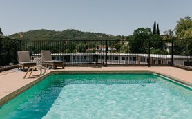 Ein klarer Pool mit grünem Wasser, umgeben von einem schwarzen Zaun und zwei Liegen, bietet einen Blick auf die Hügel.