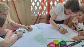 Eine Gruppe von Erwachsenen und Kindern bastelt gemeinsam Drachen, während sie an einem Tisch mit Farben und Papier arbeiten.