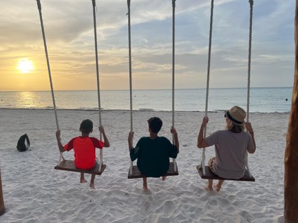 Drei Personen schwingen entspannt am Strand, während die Sonne langsam am Horizont untergeht und den Himmel in warmen Farben färbt.