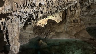 Im Inneren einer Höhle sind beeindruckende Stalaktiten und Stalagmiten zu sehen, die von sanftem Licht beleuchtet werden.