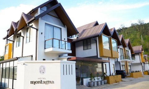Das moderne Hotel Montagna zeigt eine elegante Fassade mit schrägen Dächern und großen Fenstern, umgeben von sanften Hügeln.