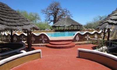 Ein einladender Poolbereich mit roten Terrassen und traditionellen Strohdächern, umgeben von üppiger Vegetation.