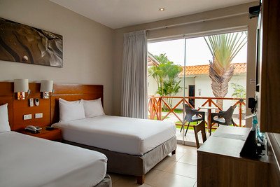Ein modernes Hotelzimmer mit zwei Einzelbetten, einem Fernseher und Blick auf einen tropischen Garten durch große Fenster.